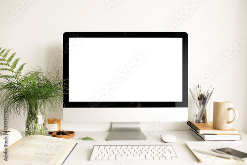 Technology, communication and electronic gadgets concept. Front view of clean stylish home office with desktop computer, open book, mug of tea, fresh fern flowers and statinary items on table