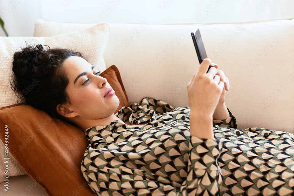 © BONNINSTUDIO/Stocksy - Young woman using smartphone on sofa