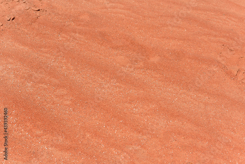 Waves of red sand. Close up of white red sand. The sand on the beach in red tones. Background with red sand in the desert.