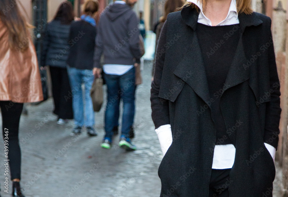 Caucasian woman in black coat and white mens shirt in the street with other people blurred. No faces. Walking in the city. Stylish fit out. City style. Classic colours. Black and white. Caucasian woman in black coat and white mens shirt in the street with other people blurred. No faces. Walking in the city. Stylish fit out. City style. Classic colours. Black and white.