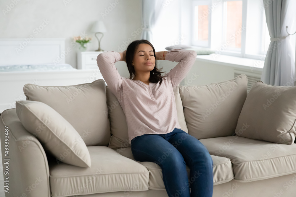 Peaceful serene African American woman resting on couch. Tired female home owner relaxing in new house living room, breathing fresh conditioning air, enjoying comfort, break, tranquility, meditation Peaceful serene African American woman resting on couch. Tired female home owner relaxing in new house living room, breathing fresh conditioning air, enjoying comfort, break, tranquility, meditation