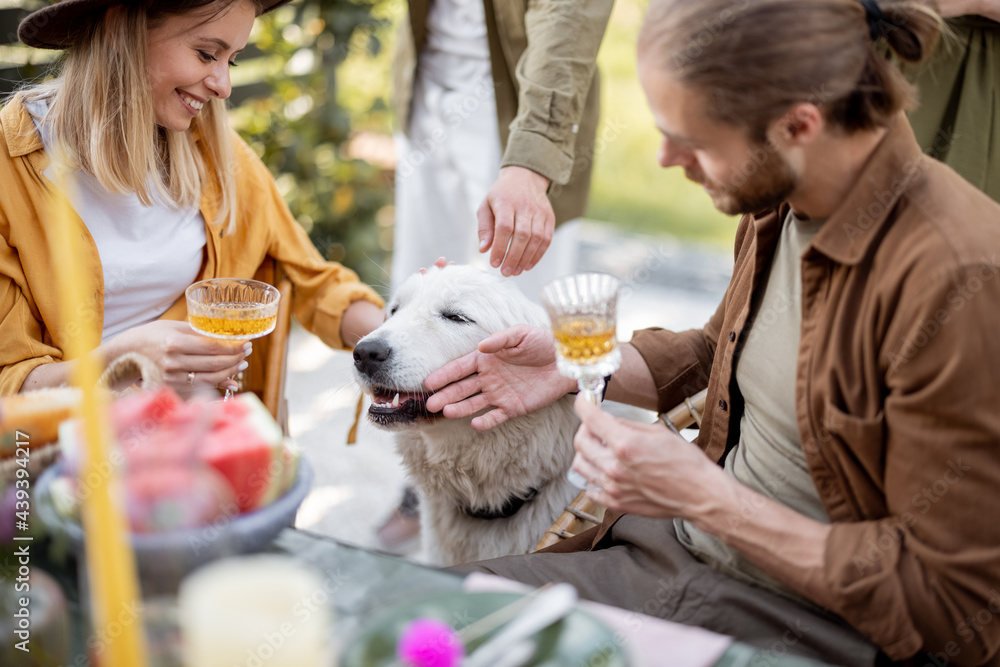 Friends playing with a dog while having a festive dinner during summertime at backyard outdoors Friends playing with a dog while having a festive dinner during summertime at backyard outdoors