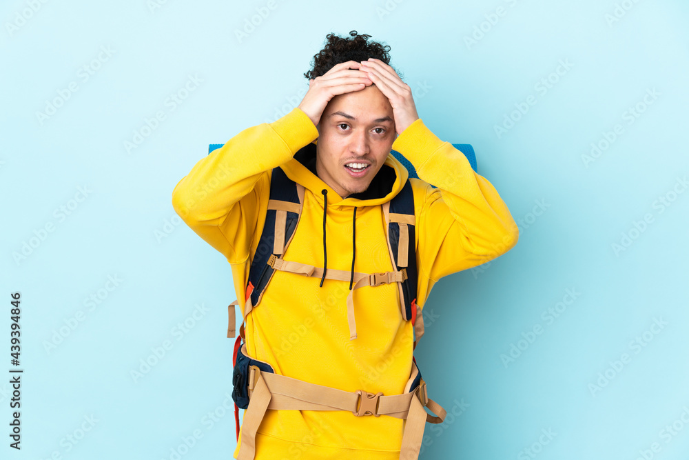 Young mountaineer man with a big backpack over isolated blue background with surprise facial expression Young mountaineer man with a big backpack over isolated blue background with surprise facial expression
