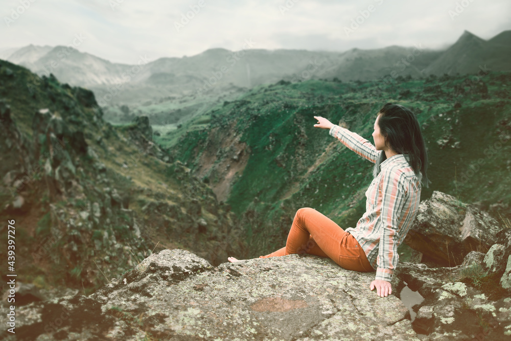 Woman tourist in the mountains points with her hand to the beauty of nature.