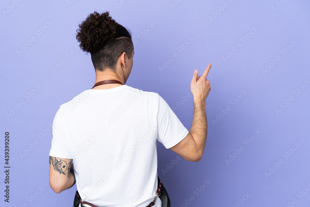 Barber man in an apron over isolated purple background pointing back with the index finger Barber man in an apron over isolated purple background pointing back with the index finger