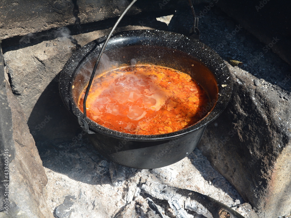 Cast iron copper hangs over an open fire. Cooking fish soup.