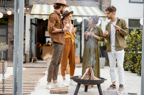 Group of young friends hang out by a fireplace, preparing for grilling at the backyard. Barbecue in close company near a country house