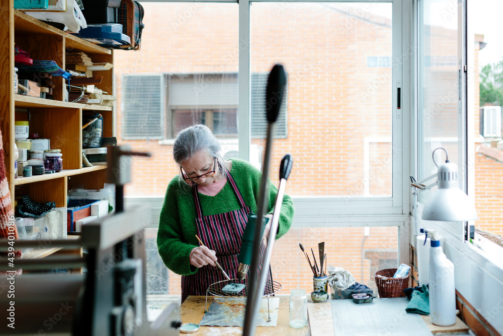 Senior woman in her bright sculptor studio working on a small bronze piece Senior woman in her bright sculptor studio working on a small bronze piece