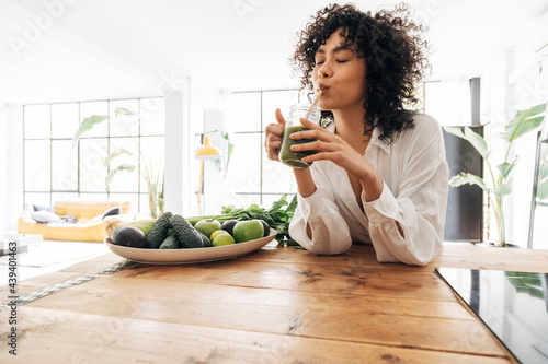 Young african american woman drinking green juice with reusable bamboo straw in loft apartment photo