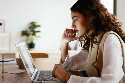 Female employee thinking over data on laptop photo