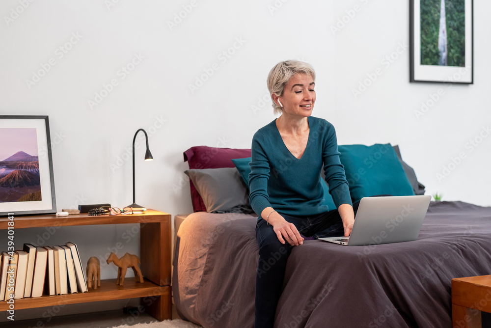Middle aged woman having a videoconference on bed Middle aged woman having a videoconference on bed