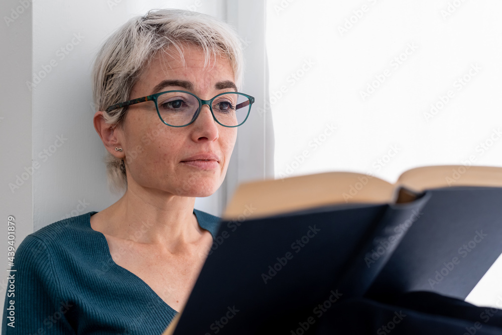 Mature woman reading book near window Mature woman reading book near window