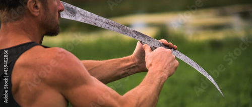 Фотография Cropped view of muscular farmer sharpening  handle scythe, banner