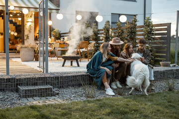 Four young friends playing with a dog, spending time together on a porch of a country house on the evening