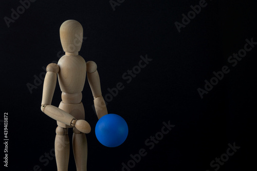 A wooden dummy holds a blue ball. Black background, close-up, copy space, horizontal orientation.