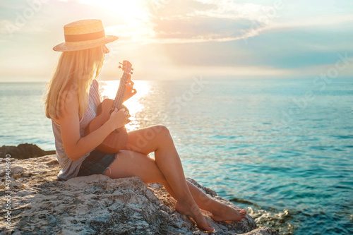 Summer Vacation. Smellingcaucasian women relaxing and playing on ukulele on beach, so happy and luxury in holiday summer, outdoors sunset sky background. Travel and lifestyle Concept. photo