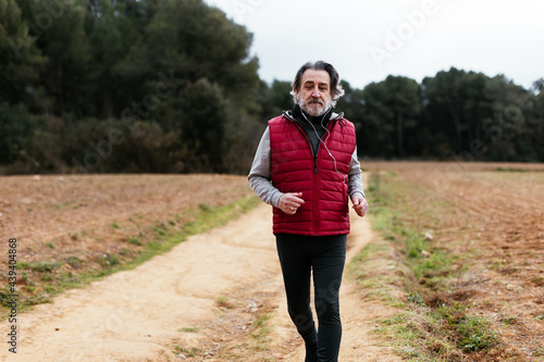 Mature jogger listening to music and running on countryside road photo