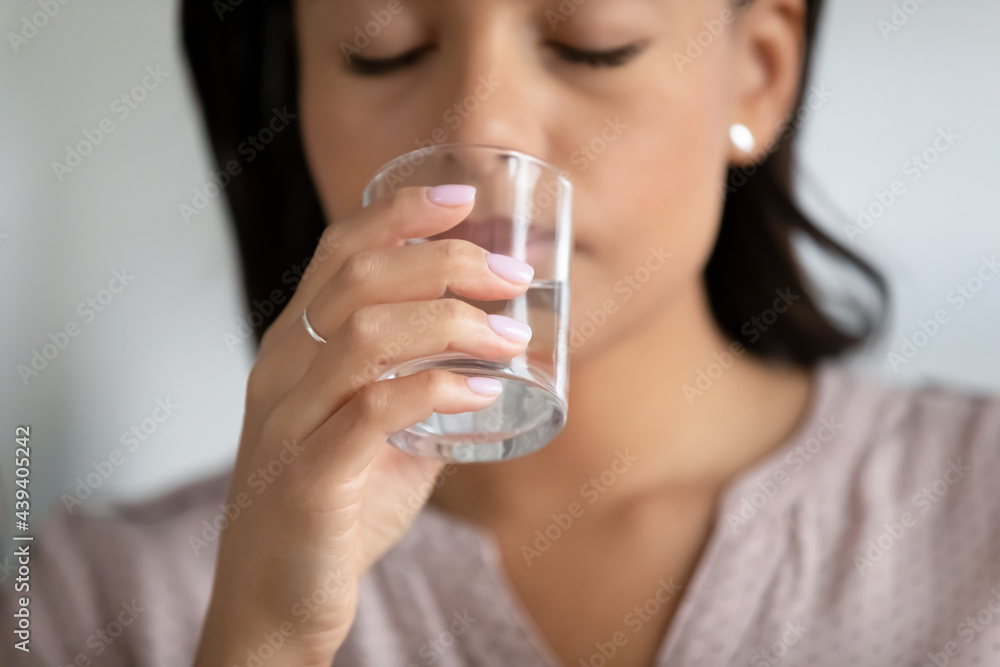 Hand of woman holding transparent glass of pure water at mouth, drinking with closed eyes, feeling thirsty, unwell, tired, taking pills. Healthy metabolism, diet, dehydration concept. Close up Hand of woman holding transparent glass of pure water at mouth, drinking with closed eyes, feeling thirsty, unwell, tired, taking pills. Healthy metabolism, diet, dehydration concept. Close up