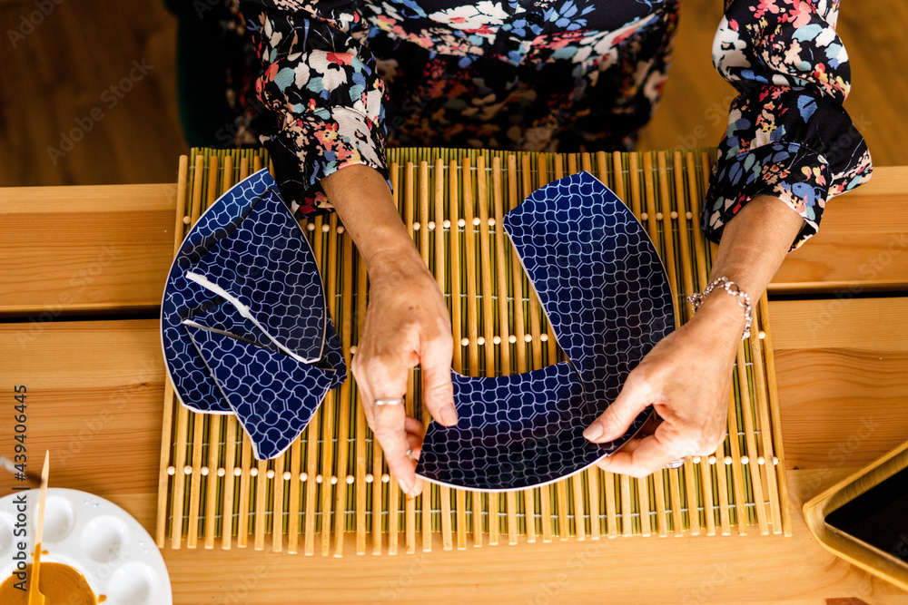 Top view of woman repairing a broken plate with gold Photos Adobe Stock