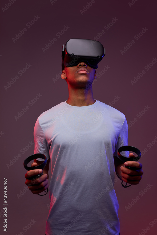 young afro american guy play VR games in virtual reality helmets on bright  colourful background, hold