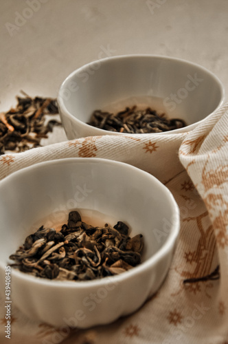 Pile of dried green tea leaves in little bowls, white background, dried tea leaves