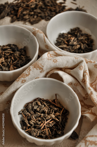 Pile of dried green tea leaves in little bowls, white background, dried tea leaves