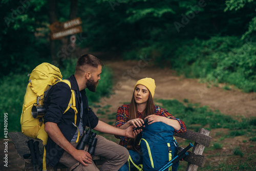 Hikers taking a break while sitting on a bench in a forest and using a smartphone