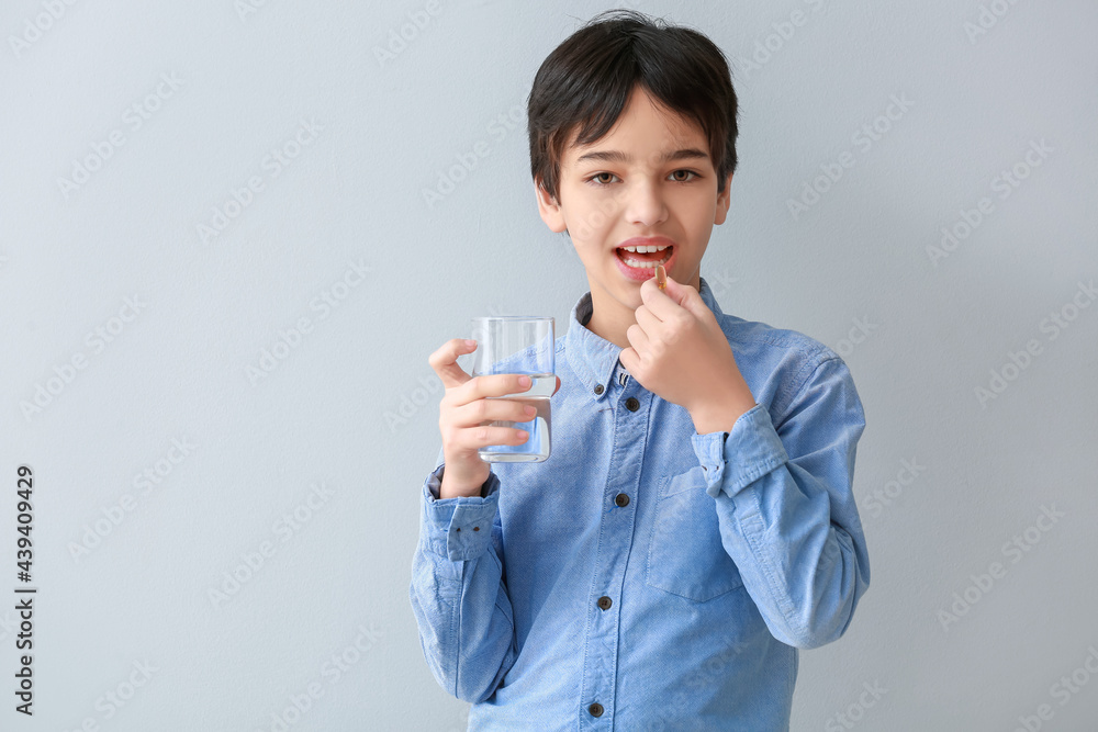 Little boy taking fish oil pill on light background Little boy taking fish oil pill on light background