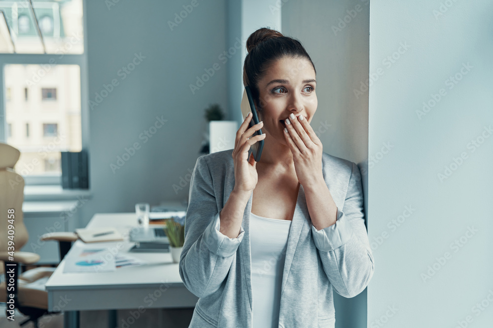 Beautiful young woman in smart casual talking on the phone and covering mouth Beautiful young woman in smart casual talking on the phone and covering mouth