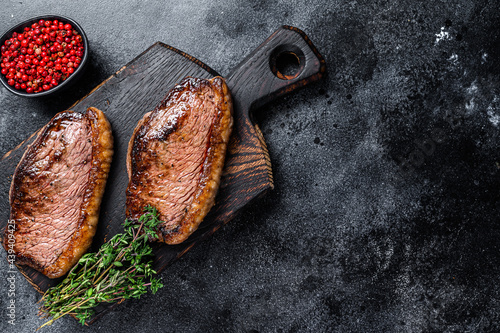 BBQ Grilled top sirloin cap or picanha steak on a wooden cutting board. Black background. Top view. Copy space