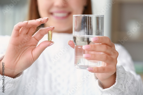 Young woman with fish oil pill at home, closeup