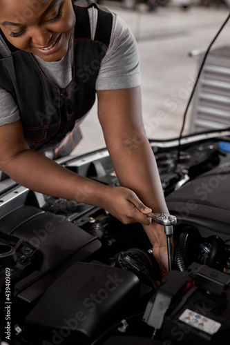 african american woman professional master repairing car in workshop at workplace, inspecting the hood of car, wearing overalls. copy space. automobile, cars, vehicle conceptt