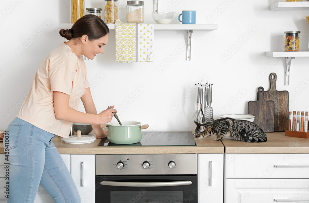 Beautiful young woman with cute cat cooking in kitchen Beautiful young woman with cute cat cooking in kitchen
