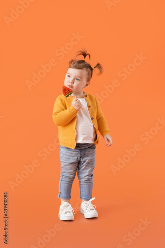 Cute little girl eating lollipop on color background