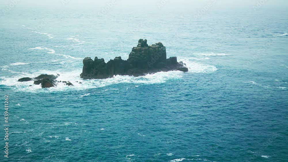 Stunning rocky island in the middle of a blue crystal ocean by cliffs in 4K. Scenic landscape view of powerful sea water waves crashing into a granite island in Cornwall, England, the United Kingdom. Stunning rocky island in the middle of a blue crystal ocean by cliffs in 4K. Scenic landscape view of powerful sea water waves crashing into a granite island in Cornwall, England, the United Kingdom.