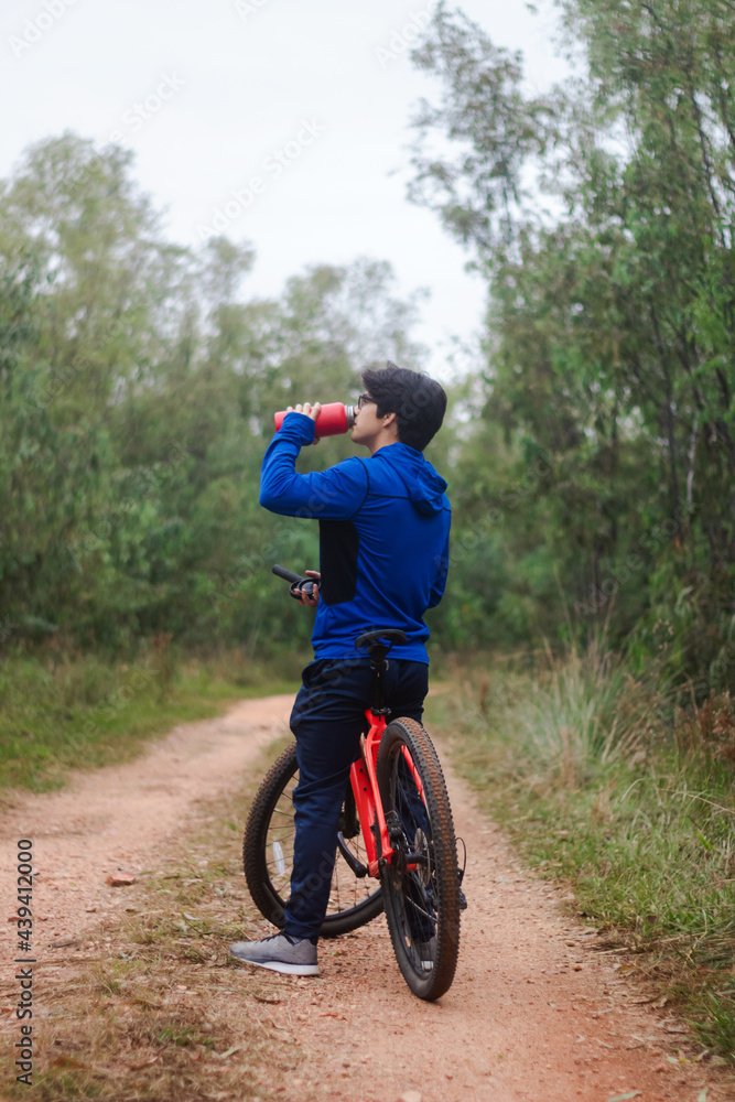 Young man drinking water on his bike on a forest road, playing sports in nature, active lifestyle. Young man drinking water on his bike on a forest road, playing sports in nature, active lifestyle.