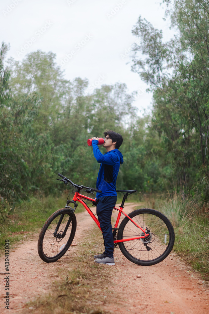 Young man drinking water on his bike on a forest road, active lifestyle.