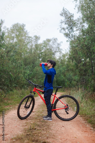 Young man drinking water on his bike on a forest road, active lifestyle.