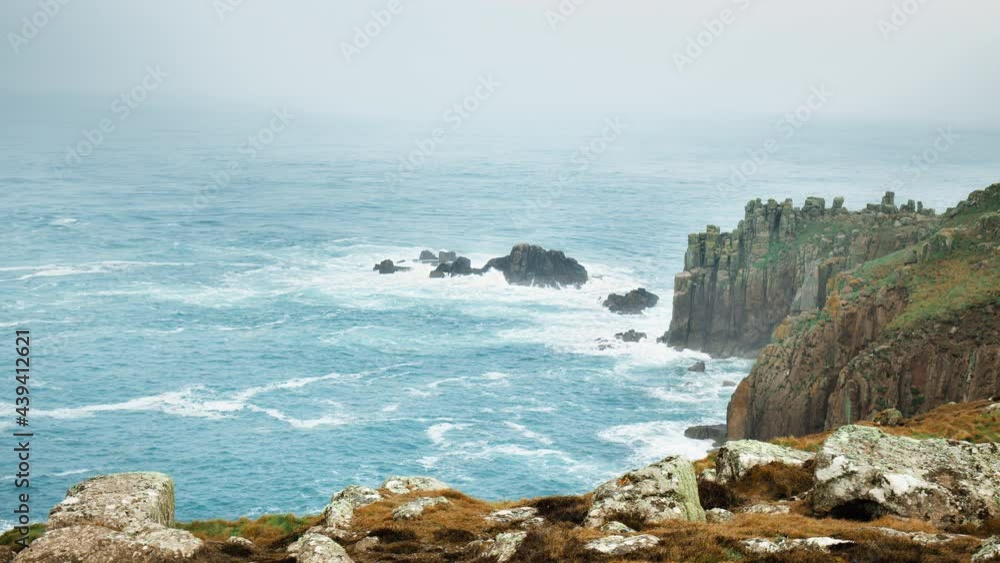 Stunning rocky island in the middle of a blue crystal ocean by cliffs in 4K. Scenic landscape view of powerful sea water waves crashing into a granite island in Cornwall, England, the United Kingdom. Stunning rocky island in the middle of a blue crystal ocean by cliffs in 4K. Scenic landscape view of powerful sea water waves crashing into a granite island in Cornwall, England, the United Kingdom.