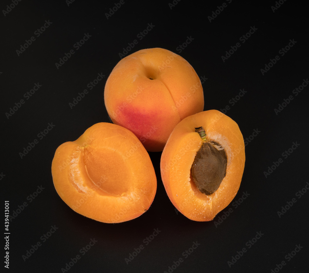 Ripe Apricot fruits, one whole apricot and two divided apricot pieces, on a black background in isolation Ripe Apricot fruits, one whole apricot and two divided apricot pieces, on a black background in isolation