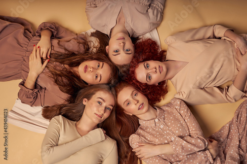 Group of beautiful models, friends, sisters with long natural red hair lay on beige background, look at camera. Attractive young models. Top view portrait. Hair care, skincare, beauty conception