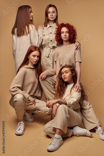 Caucasian redhead models in fashion week outfits posing together isolated on beige background. Photostudio. Fashion style. Elegant and sexy. Redhead model, beautiful face, nude make up