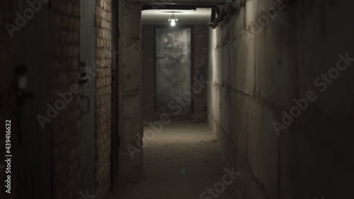 Empty scary dark hallway, cellar with concrete, brick walls with closed door. Old electrical lamps on ceiling. Black bomb shelter at the old industrial factory. Inside view.
