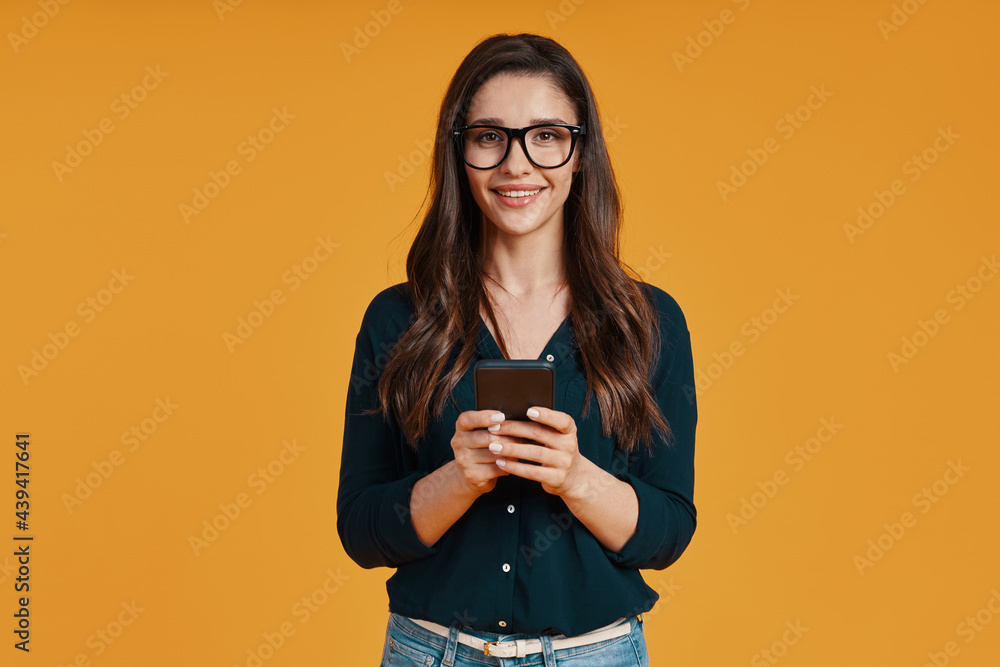 Beautiful young woman in casual clothing smiling and using smart phone Beautiful young woman in casual clothing smiling and using smart phone