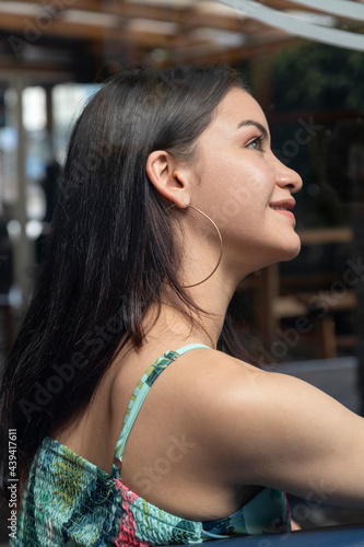 detail of the profile face of a young beautiful woman with straight and straight hair  she is smiling and wearing hoop earrings  beauty