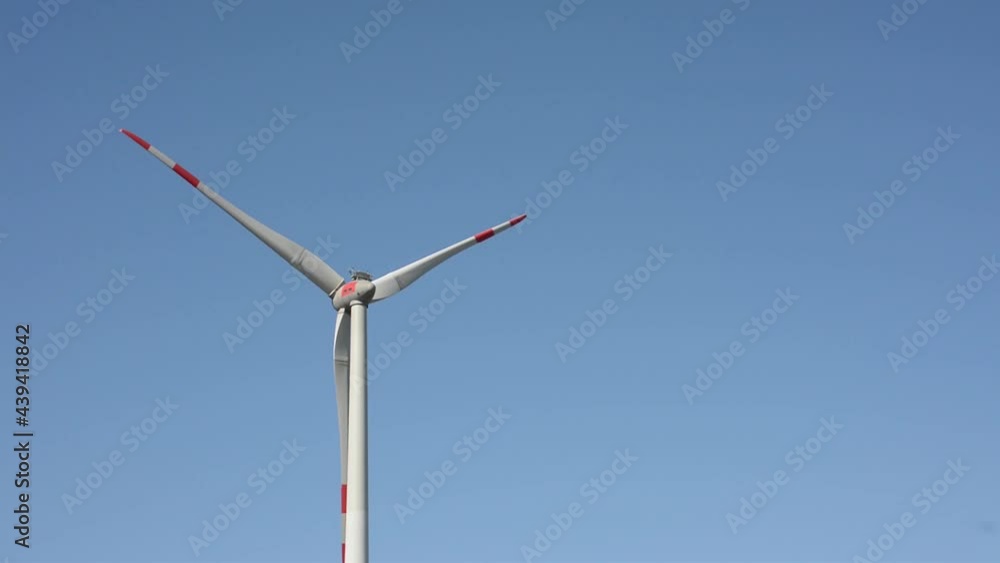 Windmill in white with red safety marks on the blades, slowly turning around on a clear blue sky 