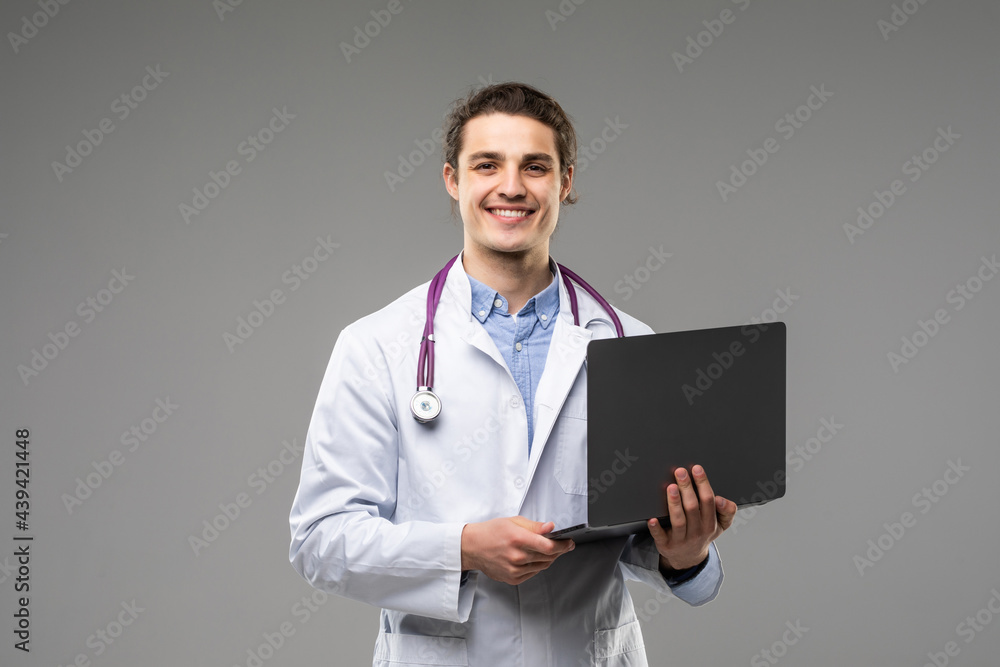 Concentrated male doctor using laptop over grey background. Concentrated male doctor using laptop over grey background.