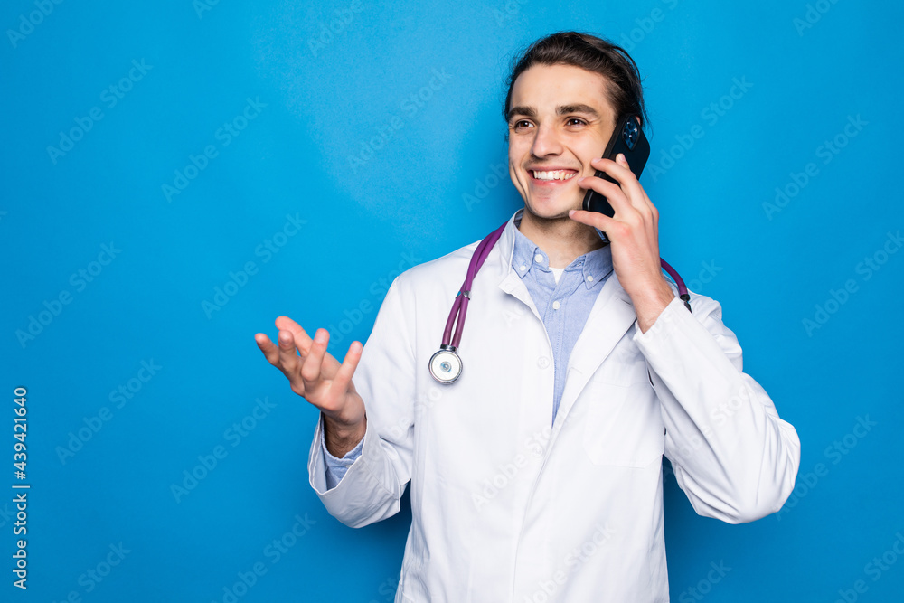 Medical doctor wearing white coat and stethoscope talking on phone standing isolated over blue background Medical doctor wearing white coat and stethoscope talking on phone standing isolated over blue background
