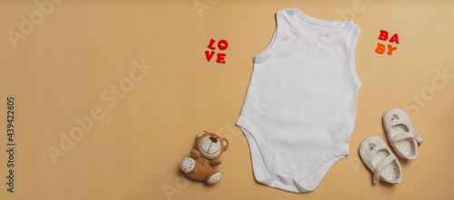 Baby clothes mockup template blank white jumpsuit for newborns, shoes and teddy bear on beige background. Space for text, top view. Banner