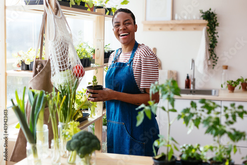 Happy black woman with potted plant standing near shelf
